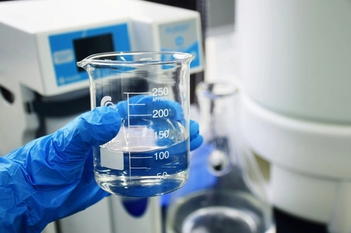 hand with blue gloves holding a beaker filled with clear liquid