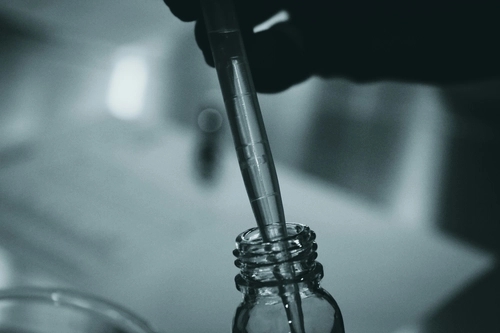 a person using a pipette to extract a clear liquid from a small vial